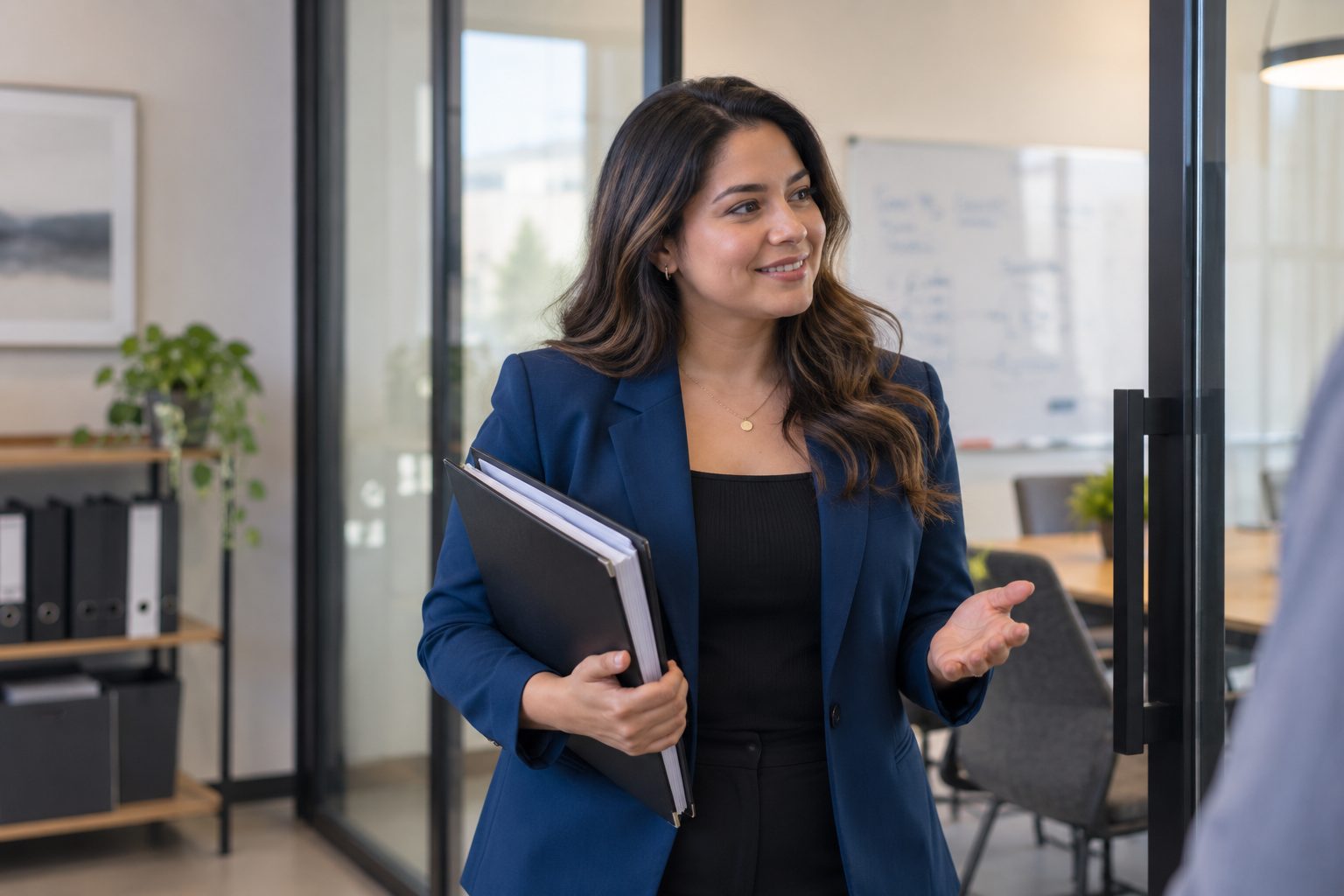 Business administrator with a binder speaking with a colleague at a meeting room doorway